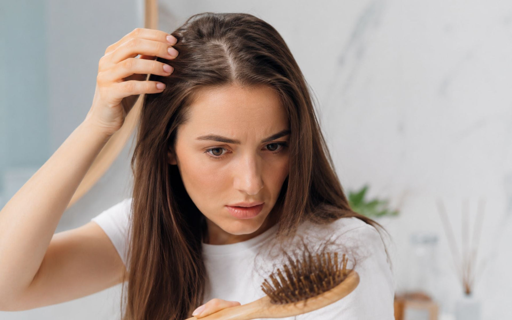 Jeune femme observant une perte de cheveux diffuse devant un miroir, tenant une brosse contenant plusieurs cheveux, illustration des symptômes pouvant être associés à une carence en fer.