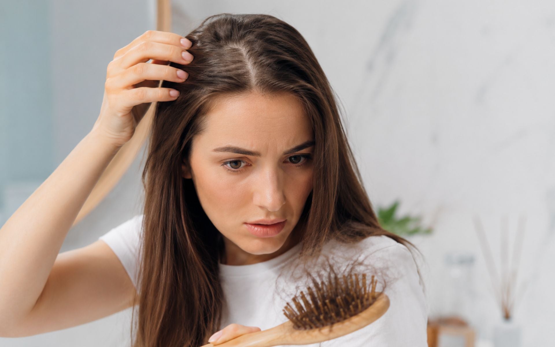 Jeune femme observant une perte de cheveux diffuse devant un miroir, tenant une brosse contenant plusieurs cheveux, illustration des symptômes pouvant être associés à une carence en fer.